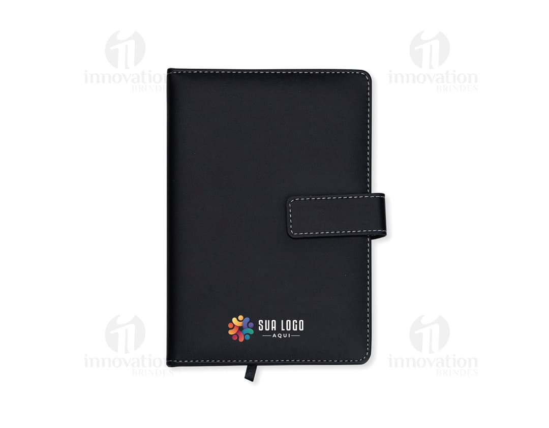 Conjunto executivo composto por notebook preto e bloco de notas de couro preto sobre uma mesa de escritório. O notebook está aberto, mostrando uma tela de dados e um teclado, junto com um dispositivo de armazenamento externo. O bloco de notas de couro está aberto, exibindo uma página em branco. Diversos itens de tecnologia, como drive externo, laptop, e disco rígido, estão presentes na imagem, juntamente com itens de papelaria, como caneta e papel. A imagem transmite uma sensação de modernidade e profissionalismo.