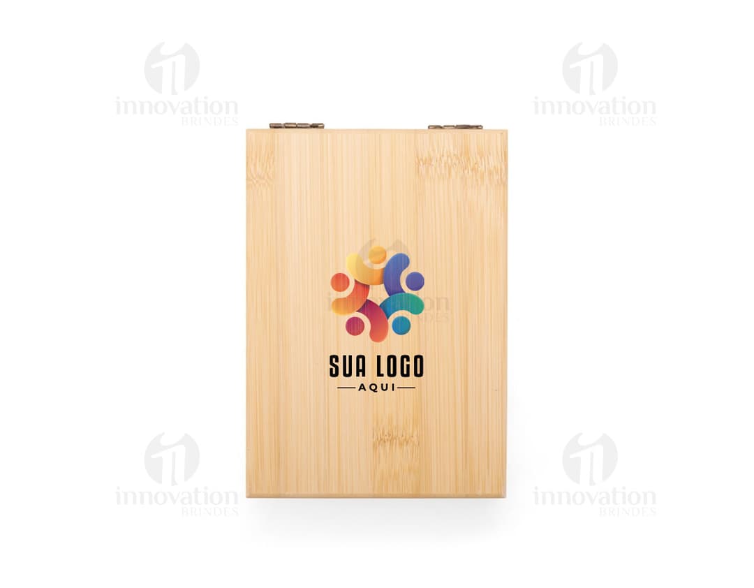 Kit vinho 2 peças em uma caixa de papelão marrom. A embalagem é de carton corrugado e contém um objeto de madeira em forma de caixa de transporte. A caixa está fechada e possui detalhes em textura de madeira. No fundo da imagem, há um bloco de madeira e vários livros empilhados.