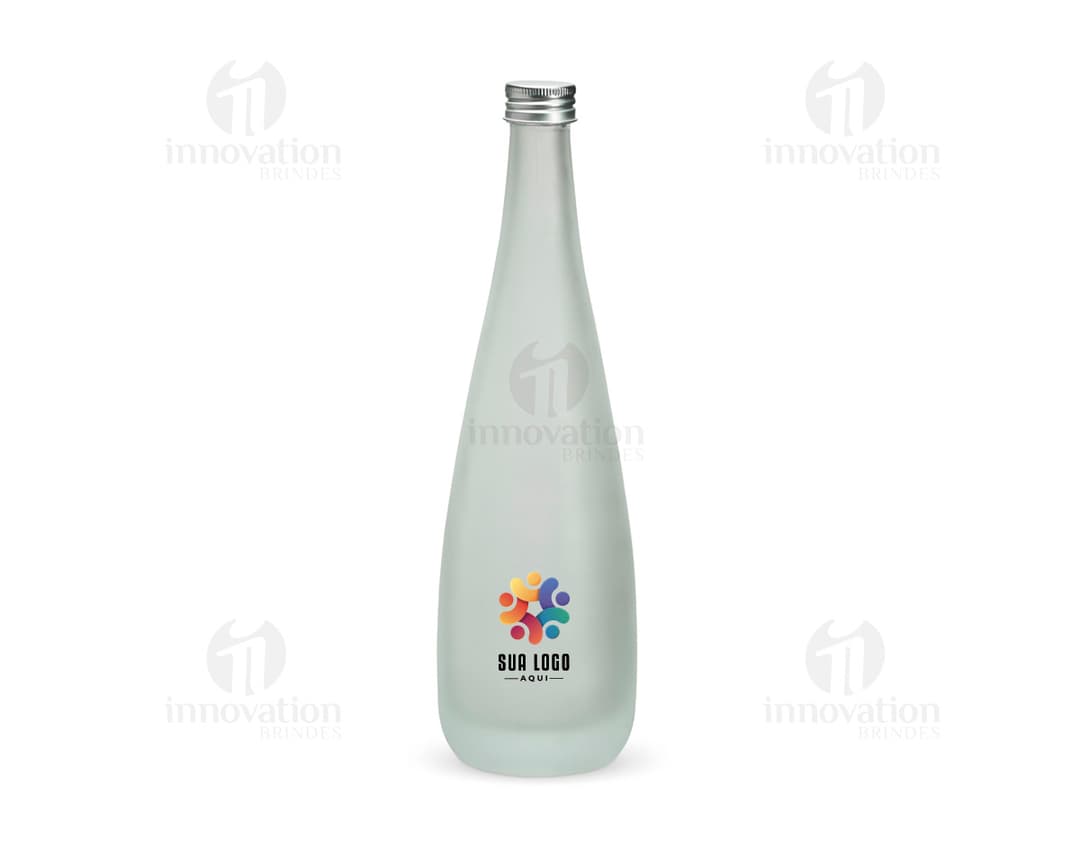 Garrafa de vidro transparente de 550ml, com label em branco. A garrafa está cheia de líquido amarelo, remetendo a uma bebida alcoólica. A imagem mostra também um copo de vidro ao lado da garrafa.