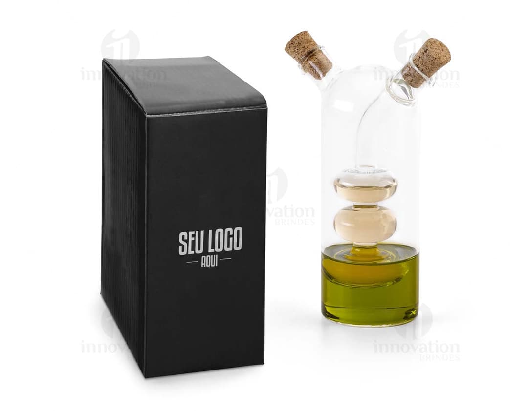 Galheteiro de vidro com três recipientes, um para azeite, outro para vinagre e um terceiro para molho de pimenta. Cada recipiente possui uma tampa de metal e um bico dosador. O galheteiro está sobre uma mesa de madeira escura.