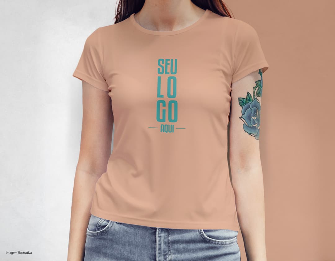 Camiseta feminina com uma garota atraente e sorridente, posando de forma casual em um estúdio. O modelo tem cabelos escuros e olhos expressivos, vestindo jeans. Ela transmite confiança e estilo.
