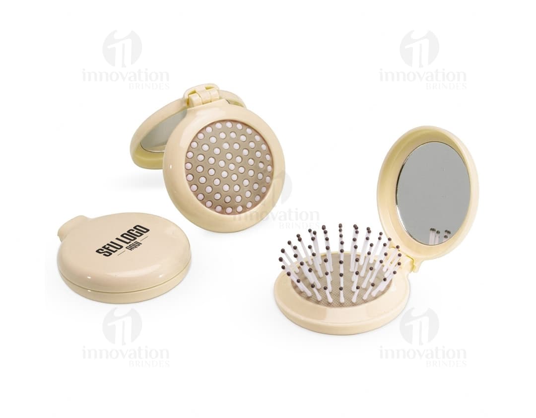 Escova com Espelho em metal prateado, design moderno e redondo, com espelho integrado. Ideal para uso como item de toiletry e maquiagem, com acabamento brilhante e símbolos em tons de preto e dourado.