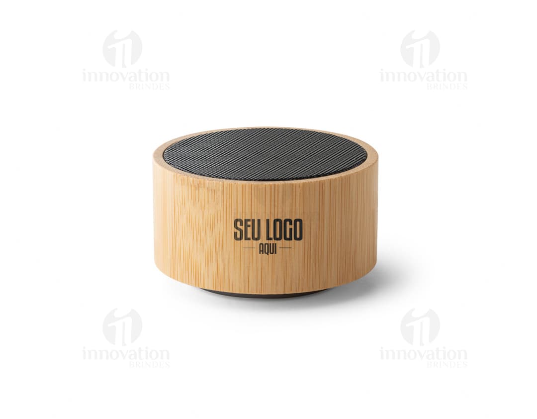 : Caixa de som de bambu e ABS com Bluetooth versão 5.0 em close-up, sobre um bloco de corte. O objeto é metálico, de cor marrom e possui empilhados muffins e cupcakes, com cobertura de chocolate e creme. O dispositivo é brilhante e reflete a luz, indicando alta qualidade.