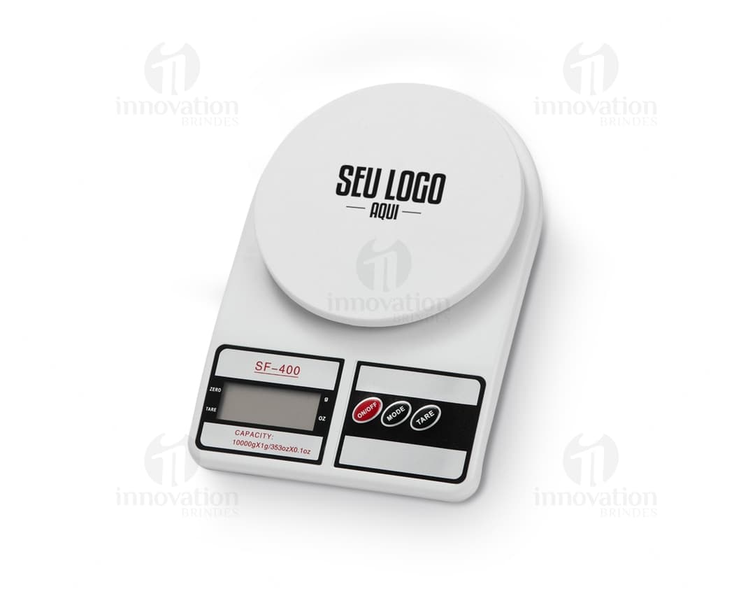 Mulher sorrindo e trabalhando em sua cozinha, com uma mesa de café da manhã com comida, xícara de café, pratos e utensílios. Ela está segurando uma balança digital para cozinha.