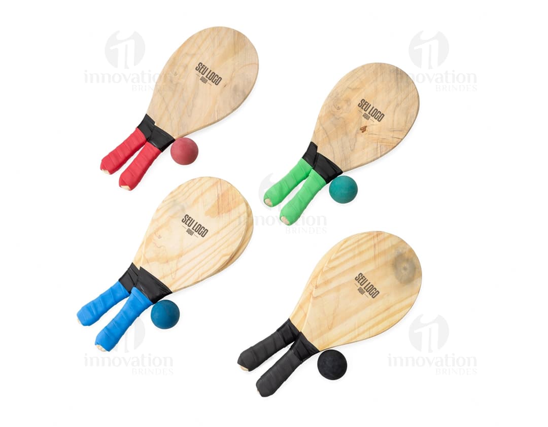 Kit Frescobol em um fundo de praia, contendo duas raquetes e uma bolinha de frescobol.