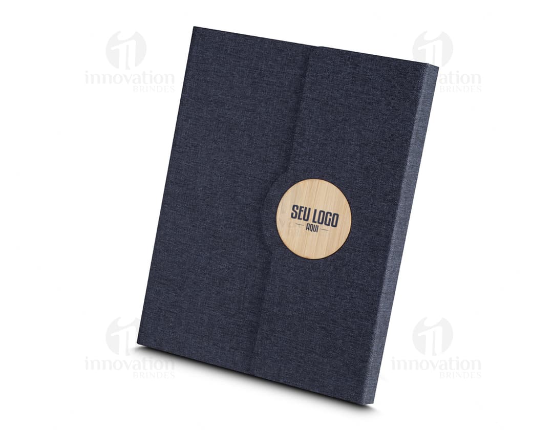 Caderno de anotações marrom com capa de couro vazia sobre uma mesa de escritório. O caderno está aberto exibindo páginas em branco e ao redor dele há um teclado de computador, um disquete, um laptop, um disco magnético, papel, uma pasta, um cartão e uma caneta. A imagem transmite uma sensação de negócios e tecnologia.