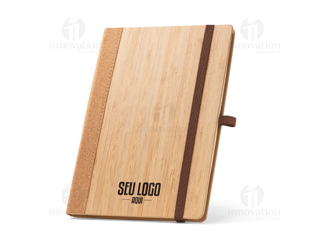 Caderno A5 de capa dura marrom com textura de madeira, feito de material de papel e contendo um instrumento de cordas e um utensílio de cozinha sobre ele. O caderno está em cima de uma tábua de corte de madeira com um afiador de lápis antigo ao lado, em um ambiente de cozinha.