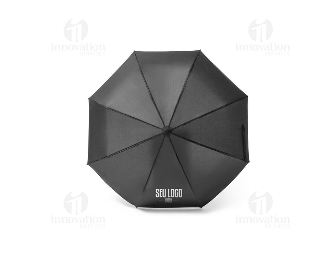 Guarda-chuva dobrável preto em formato de capelo de formatura, simbolizando sucesso e educação. O objeto 3D está aberto e vazio, sendo segurado por uma mão masculina. A imagem representa conhecimento, celebração e conquista acadêmica.