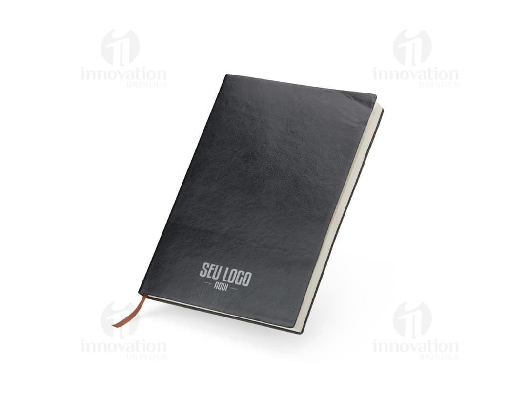 Caderneta em PU A5 na cor preta com fecho de elástico e detalhe em dourado. O produto está aberto e é possível ver as páginas em branco internas.