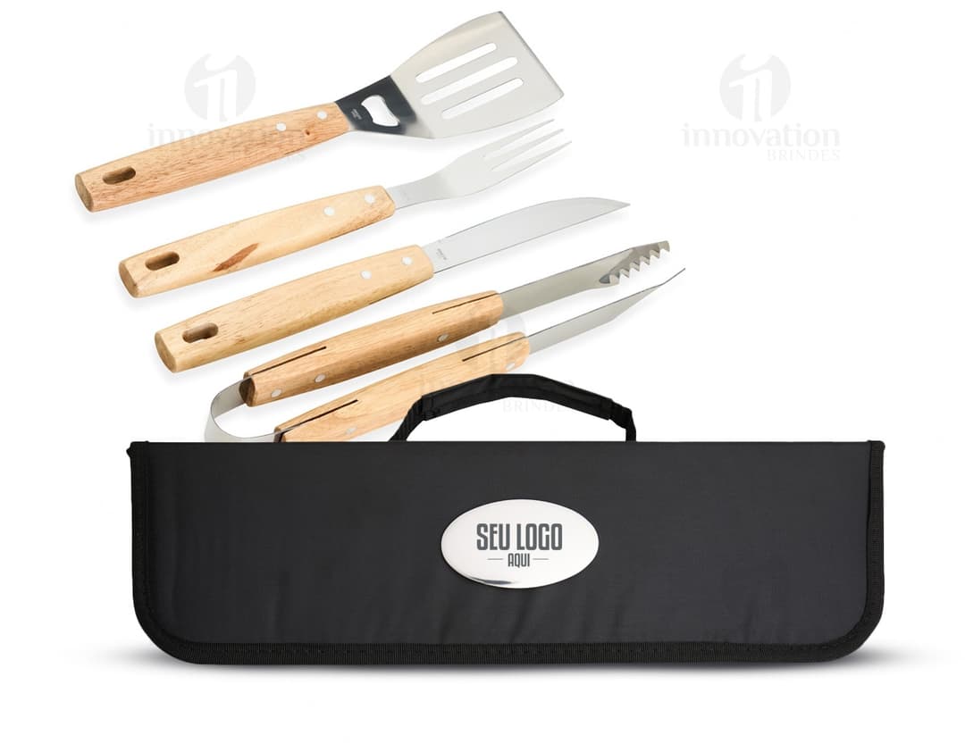 Kit churrasco contendo 4 peças de utensílios de aço inoxidável, incluindo espátula, garfo, faca e pegador. O conjunto vem em uma maleta de plástico preta, ideal para churrascos e outras atividades ao ar livre.