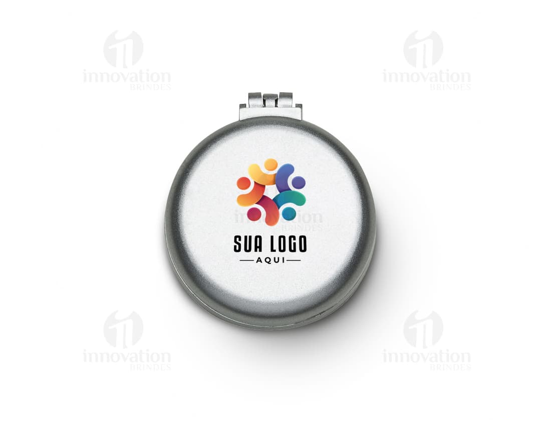 Espelho de bolsa com escova preta e vermelha, feito de vidro e metal, com um botão redondo para fechar. Possui um ícone de lupa prateada, símbolo de pesquisa e ampliação. O objeto é um instrumento de maquiagem compacto e prático para levar na bolsa, ideal para retoques durante o dia.