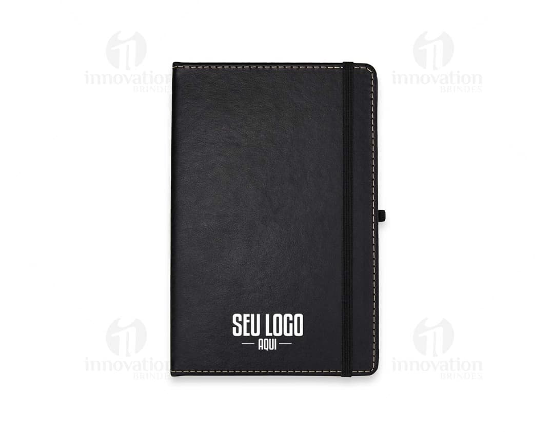 Caderneta em Couro Sintético preto com fecho magnético e papel pautado.