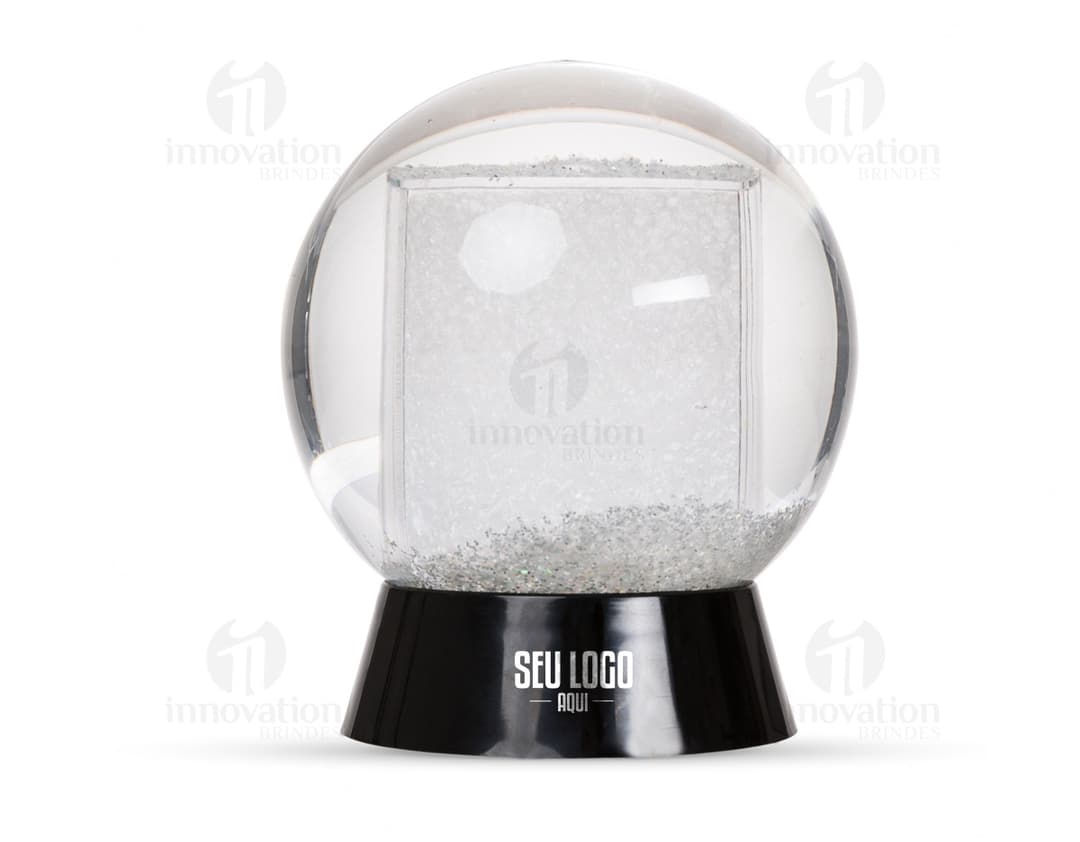 Globo de neve plástico transparente com uma paisagem de neve e uma pequena figura de um boneco de neve no centro.