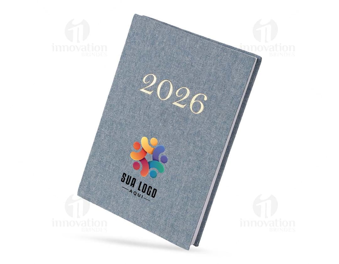 Notebook de linho para Agenda Diária 2026, com moderm à frente, equipamento eletrônico, livro, papel em branco, objetos de escritório, em destaque.