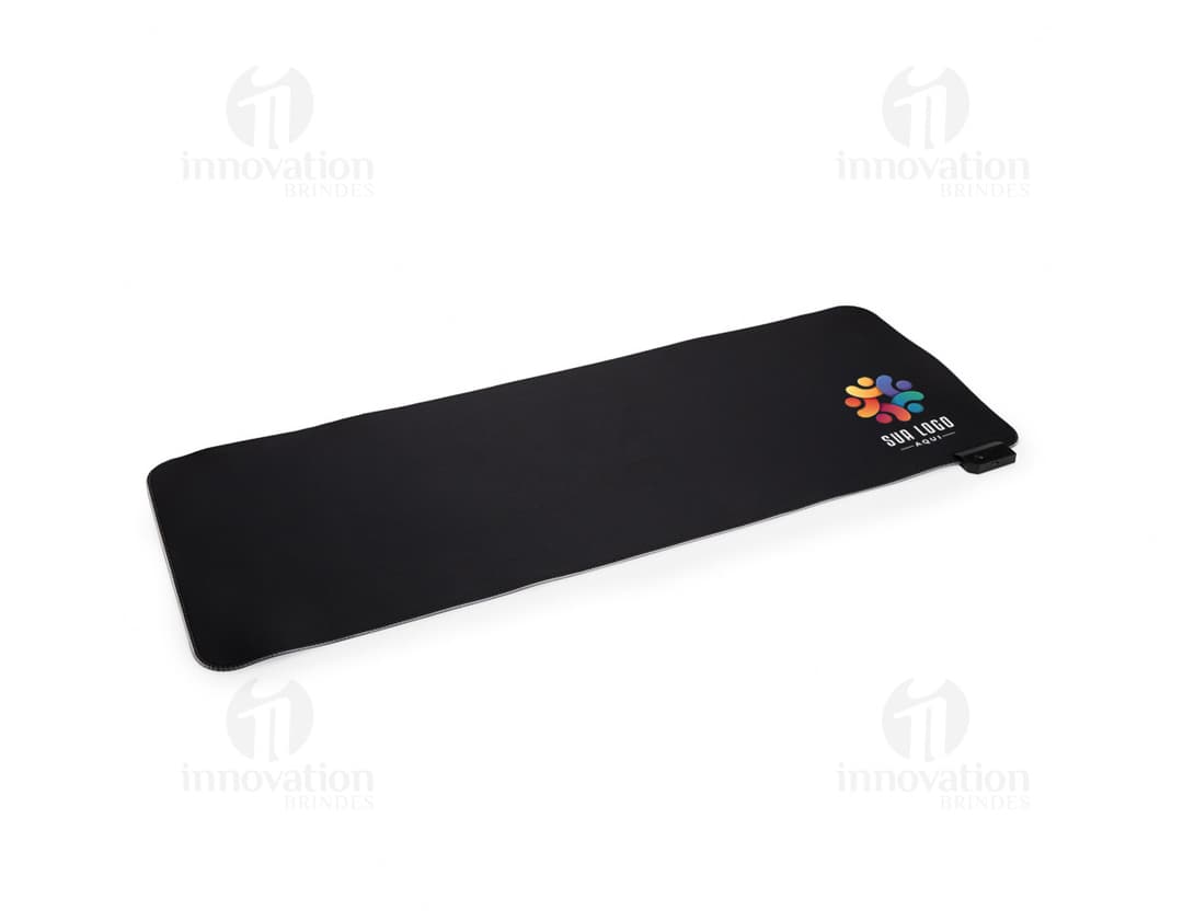 Desk Pad Microfibra com LED em formato retangular, na cor preta, com iluminação LED na parte inferior. O produto está sobre uma mesa de madeira, ao lado de um notebook e uma caneca de café.