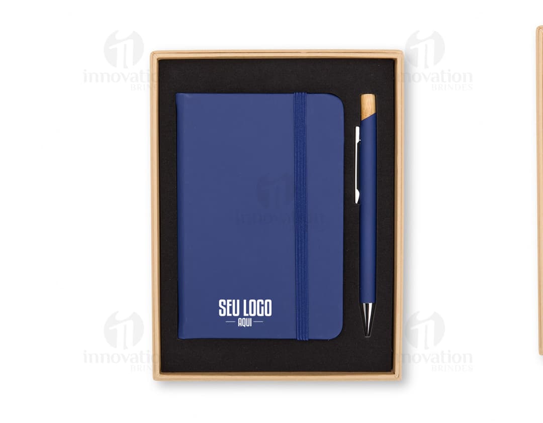 Notebook e laptop preto e prateado aberto sobre uma mesa de escritório, com tela vazia. O teclado, o mouse pad e o monitor estão visíveis. Ao lado, um notebook fechado e um celular. A imagem transmite um ambiente moderno e tecnológico.