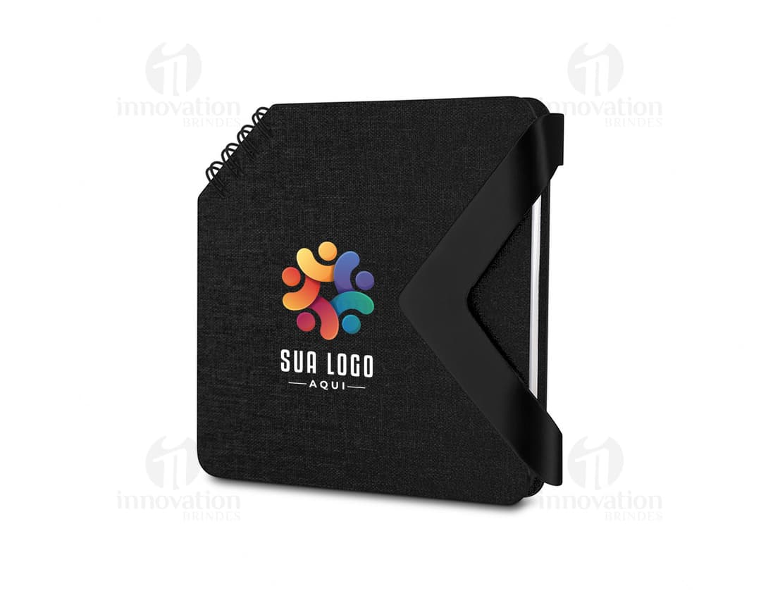 Mini caderno preto de couro aberto sobre uma mesa de escritório, ao lado de um notebook e diversos dispositivos eletrônicos. Contém páginas em branco, chave, memo, papel e ícones de segurança, representando um local para armazenar dados e informações importantes.