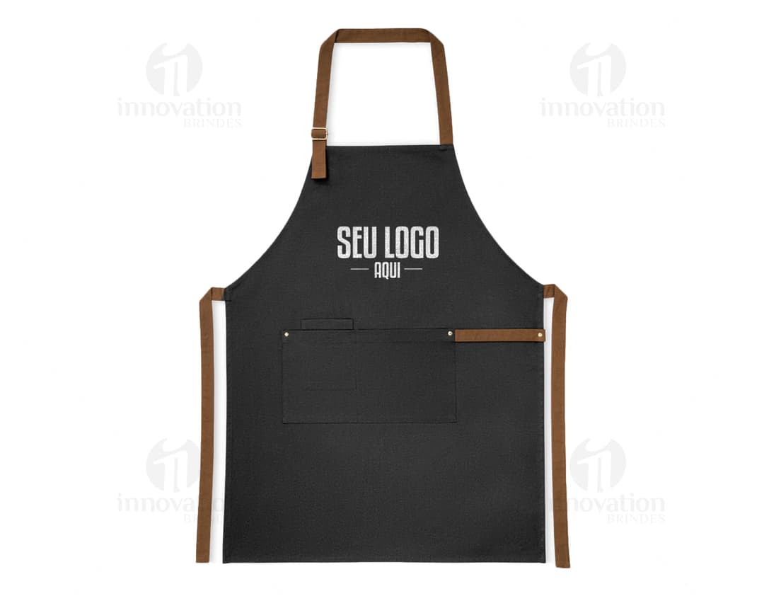 A imagem mostra um avental de algodão canvas com 300g de gramatura, com um bolso e tira de fechamento. O produto possui detalhes em metal e é ideal para uso em trabalho, tanto para homens quanto para mulheres. O avental tem um design moderno e é perfeito para quem busca praticidade e elegância ao mesmo tempo.